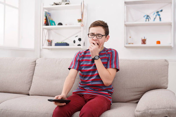 Poika katselee televisiota ja näyttää tylsistyneeltä sohvalla kotona
 - Valokuva, kuva