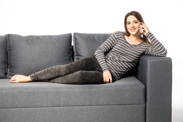 Szczęśliwa młoda kobieta rozmowy telefon komórkowy, leżąc na kanapie na białym - Zdjęcie, obraz