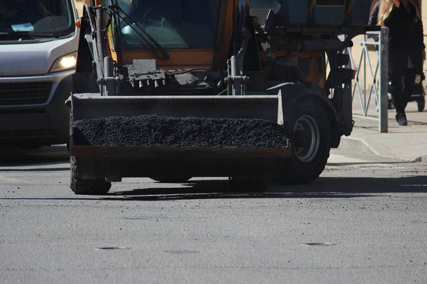 Mini excavator transports in the scoop asphalt crumbs to repair road pits in the city of st. Petersburg. - Photo, Image