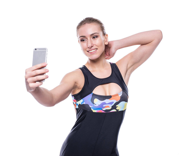 Happy fitness young woman wearing sportswear tracksuit is taking selfie with her mobile phone isolated on white background. - Fotografie, Obrázek