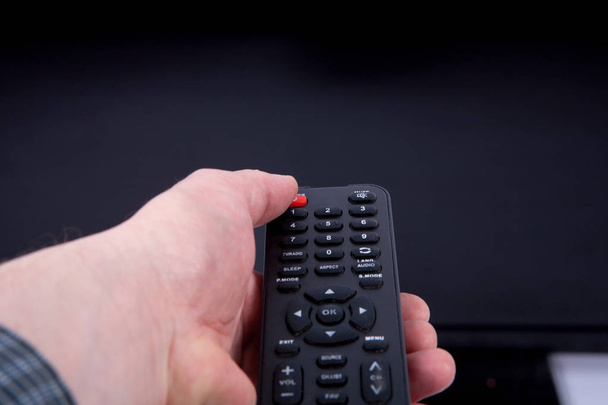 Hand using a remote control in front of the TV screen - Photo, image