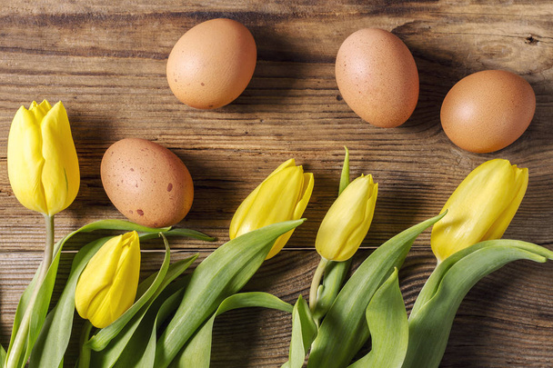 Žluté tulipány a čerstvá slepičí vejce na dřevěný stůl, pohled shora - Fotografie, Obrázek
