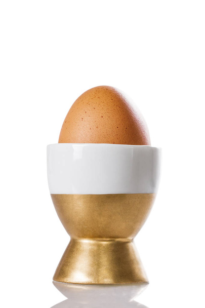 Варёное яйцо в золотой чашке, изолированной на белом
 - Фото, изображение