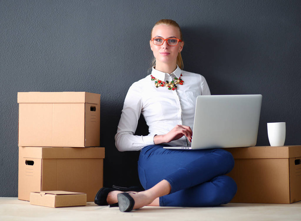 Woman sitting on the floor near a boxes with laptop - Foto, imagen