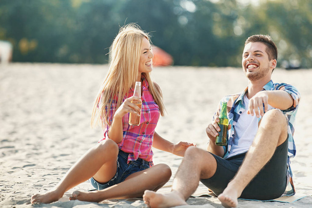 Young Couple Driniking Beer on the Beach - Фото, изображение