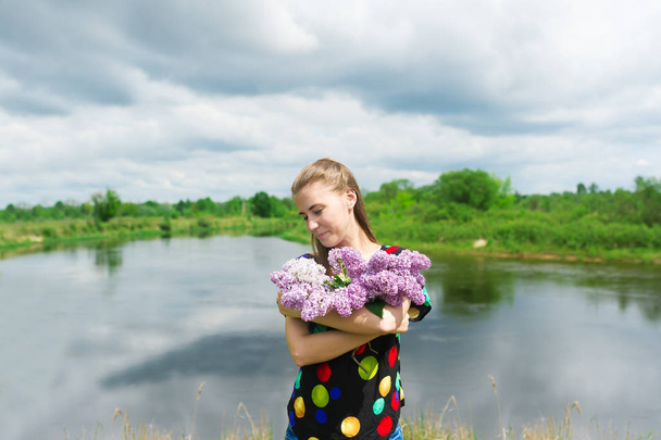 La bella ragazza su un bouquet di lilla sullo sfondo del fiume
 - Foto, immagini