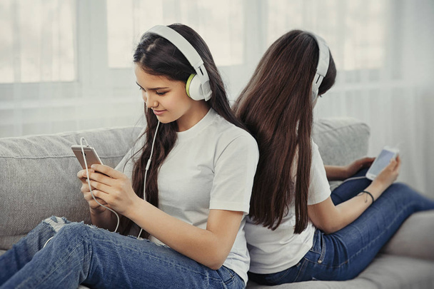 Hermanas adolescentes con teléfono inteligente y auriculares escuchando música y se comunican en las redes sociales
 - Foto, imagen