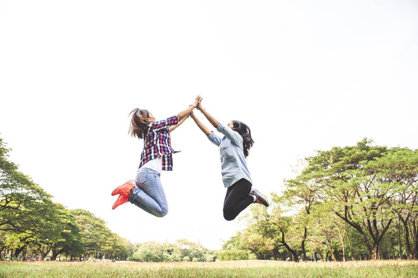 Two happiness young women jumping over sky,jumping at summer park - Foto, imagen