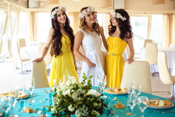 Beautiful Bride and two bridesmaids in yellow similar dresses together in a sea restaurant - Photo, Image