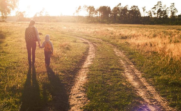 mother and son walking on the meadow at sunset, - Foto, afbeelding