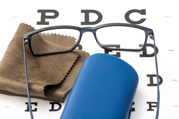 Lectura de anteojos negros, paño de limpieza de microfibra marrón y estuche protector azul sobre ojo blanco
 - Foto, Imagen