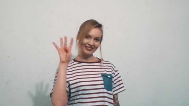 Vonzó fiatal szőke nő felhúzni négy ujja előtt fehér fal - Felvétel, videó