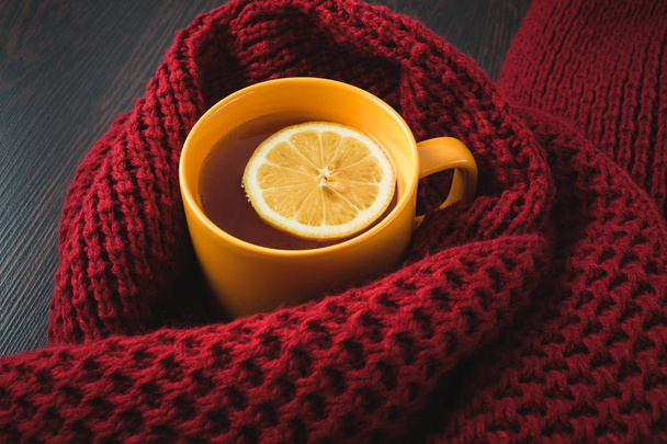 Kopje warme thee met citroen gekleed in gebreide warme winter sjaal, warme gebreide trui of deken. Stilleven van een sjaal en een kopje thee met citroen. Wintertijd. Gezellige en zachte winter achtergrond. - Foto, afbeelding