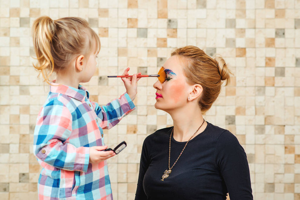 Cute little girl are doing makeup for her beautiful mother. - Foto, Imagen