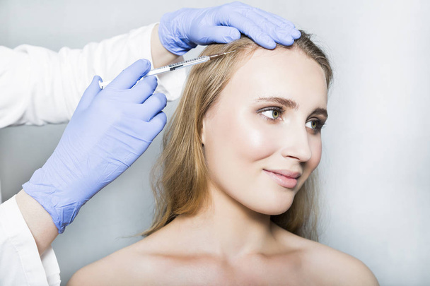 Doctor aesthetician makes head beauty injections to female patient on white background - Foto, afbeelding
