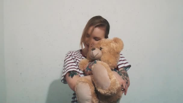 Mujer rubia linda en camisa a rayas con tatuajes, abrazos con juguete de oso de peluche
 - Metraje, vídeo
