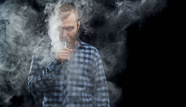 Vaping man holding a mod. A cloud of vapor. Black background. Studio shooting. - Valokuva, kuva