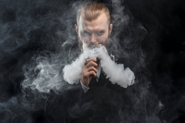 Vaping man holding a mod. A cloud of vapor. Black background. Studio shooting. - Foto, immagini