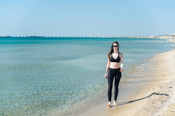 A young girl walks along the beach after a run in sunglasses - Foto, Imagem