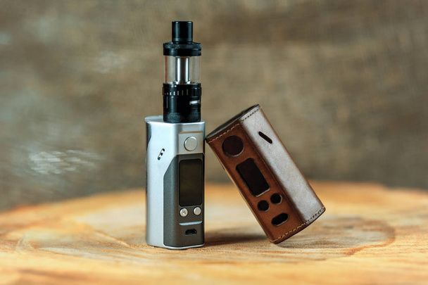 Vape. An electronic cigarette mod and leather case on a wooden table. - Zdjęcie, obraz