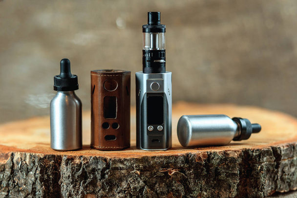 Vape. An electronic cigarette mod, leather case and two aluminum bottles with e-liquid on a wooden table. Personal vaporizer. - Foto, afbeelding