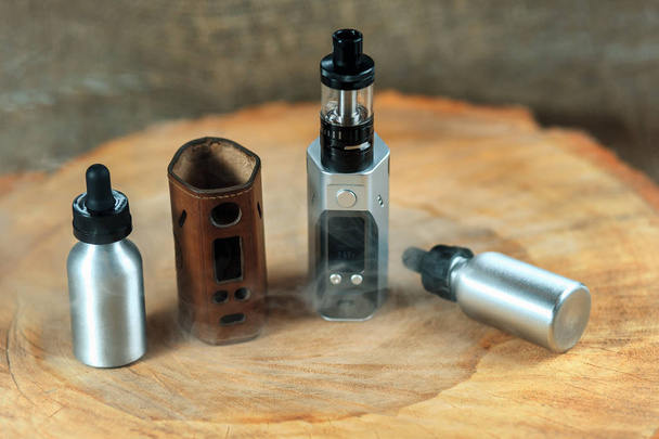 Vape. An electronic cigarette mod, leather case and two aluminum bottles with e-liquid on a wooden table. Personal vaporizer. - Foto, imagen