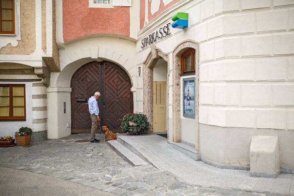 An elderly man with a dog at the building of Savings bank. Village Weissenkirchen, Lower Austria. - Foto, imagen
