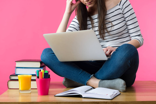 attraktive kaukasische Mädchen studiert für ihre Prüfungen zu Hause, Studentin sitzt auf ihrem Schreibtisch mit Laptop auf dem Schoß - Foto, Bild