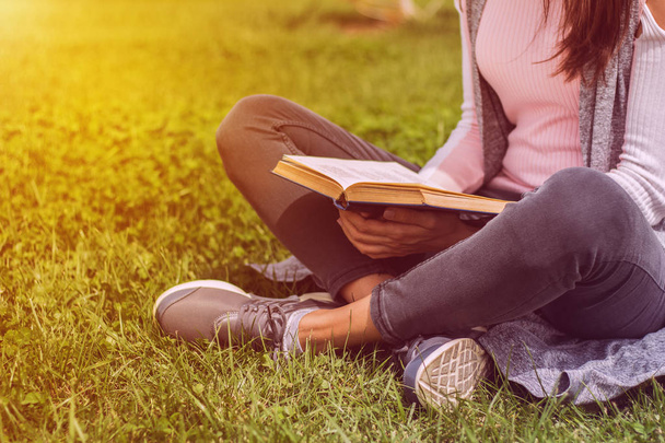 Young girl reading book sitting on green grass in park on meadow - Foto, afbeelding