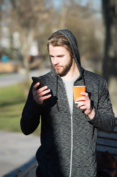 young man holds coffee, tea paper cup, phone in jersey - Foto, Imagen