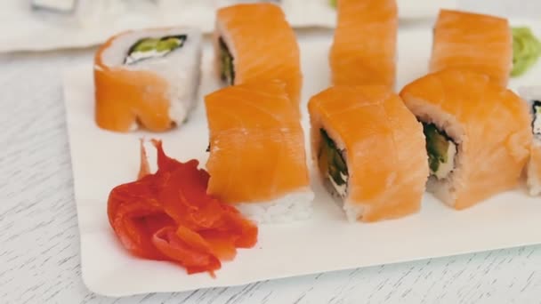 Νόστιμο σούσι, με σολωμό, τυρί, wasabi, ροζ τζίντζερ, σάλτσα σόγιας για ένα κομψό λευκό φόντο ξύλινη - Πλάνα, βίντεο