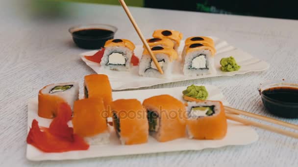 Herkullinen sushi lohen, juuston, wasabin, vaaleanpunaisen inkiväärin, soijakastikkeen kanssa, jotka on otettu puisilla tikkuilla tyylikkäällä valkoisella puupohjalla
 - Materiaali, video