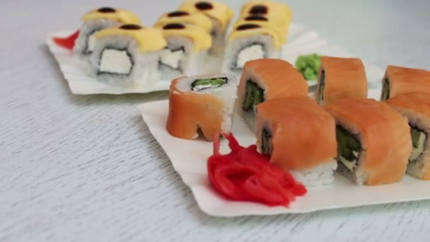 Świeże, pyszne sushi z imbirem łososia i sera i wasabi na białych talerzach w kawiarni - Materiał filmowy, wideo
