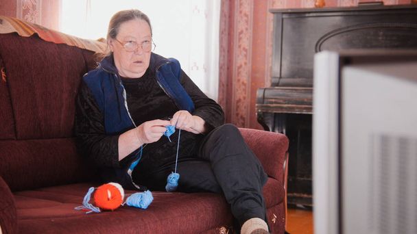 Stará dáma doma na pohovce - starší žena, sledování televize a plete vlny ponožky - Fotografie, Obrázek