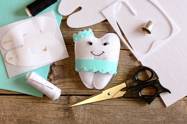 Nice felt tooth fairy pillow, paper template, felt sheets and scraps, scissors, thread on vintage wooden background. Handmade felt tooth fairy pillow for children. Stitching concept. Top view. Closeup  - Photo, Image