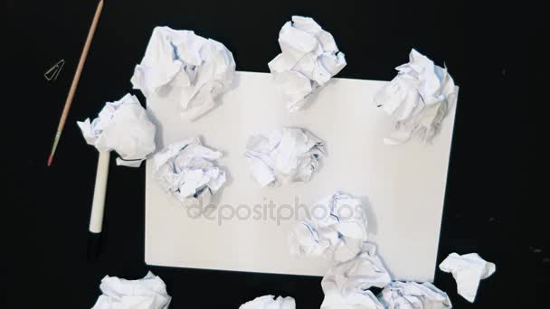 Hand sweeps away crumpled paper and writing accessories off black table - Footage, Video