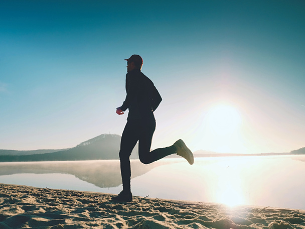 Силует спортивної активної людини, що бігає на пляжі озера на сході сонця. Здоровий спосіб життя
.  - Фото, зображення