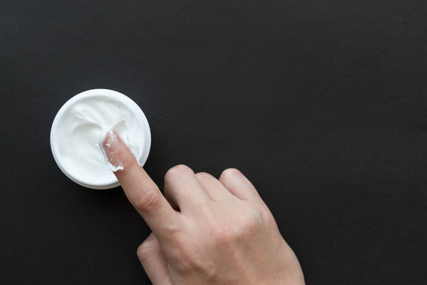 Crema para cara o cuerpo en recipiente blanco y mano femenina en bla
 - Foto, Imagen
