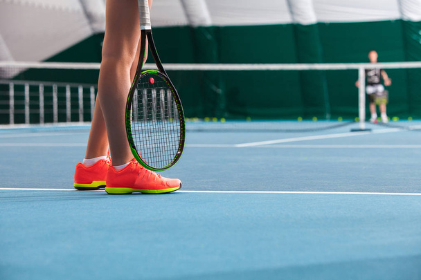 Legs of young girl in a closed tennis court with ball and racket - Valokuva, kuva