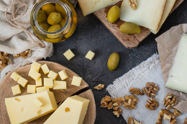 ハード チーズ (スウェーデン、スペイン マンチェゴ、イタリアのペコリーノ トスカーノ) のさまざまな種類のチーズの盛り合わせ薄切りし、ガラスの瓶とクルミのグリーン オリーブをみじん切り - 写真・画像