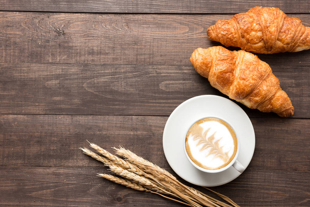 Coffee cup and fresh baked croissants on wooden background. Top  - Foto, afbeelding