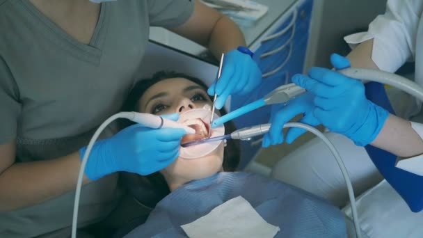 Young woman sitting in the dental chair with opening wide mouth. Dentist with nurse clean and polish teeth. - Filmmaterial, Video
