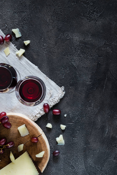 Two glasses of red wine, chopped Spanish hard cheese manchego on wooden cut with red grapes - Foto, afbeelding