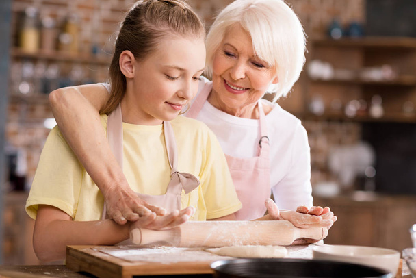 Grand-mère et petit-enfant pétrissant la pâte
  - Photo, image