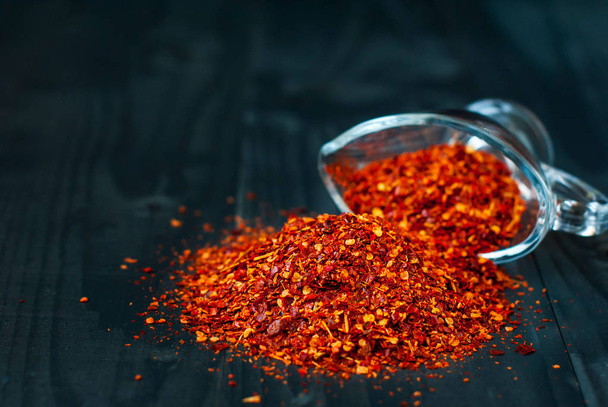 Ground chilli pepper on a dark background. Spicy chili is scattered on a wooden table. - Fotó, kép