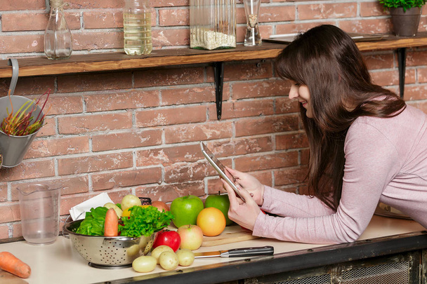 Chica mira la tableta.Mujer joven Cocinando en la cocina en casa. Comida saludable
. - Foto, imagen