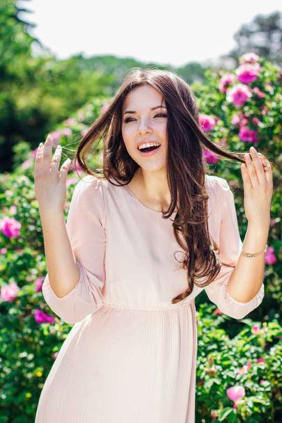 Outdoor fashion photo of beautiful young happy smiling woman surrounded by flowers. Spring blossom - Foto, Bild