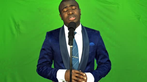 junger afrikanischer Mann singt vor grünem Hintergrund und blickt in die Kamera. - Filmmaterial, Video