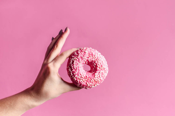Hand Holding colorful donut with sprinkles on a wooden table and pink background. Two types of donuts. Cake and sweet. Food detail. Close up. Pastel color - Foto, Imagem