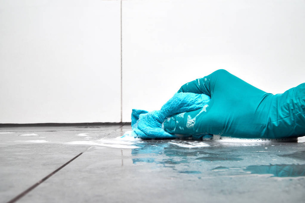 Male hand witha blue rag cleaning the bathroom tiles on the floor. - Photo, image